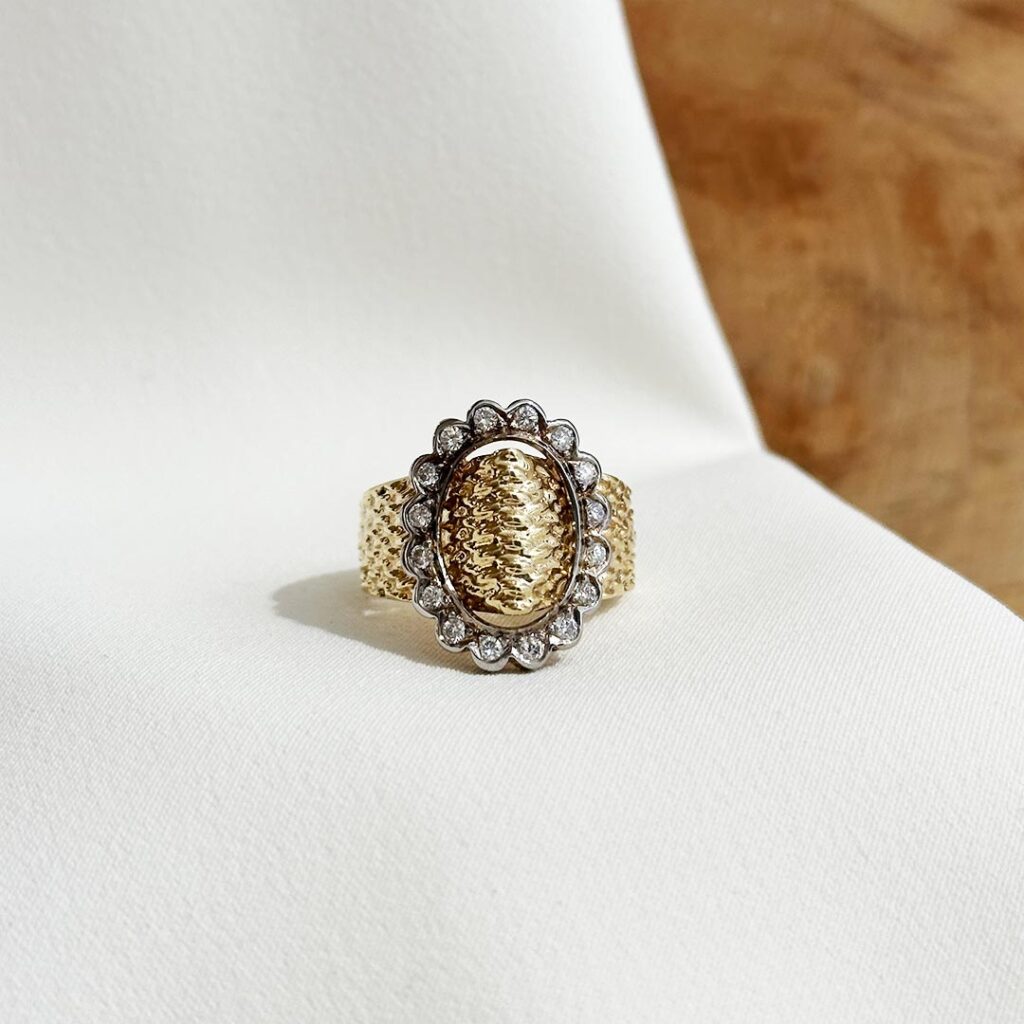 Auffälliger Ring aus Gelbgold mit funkelnden Brillanten in Weißgoldfassungen, markantes Design und starker Kontrastwirkung, in eleganter Nahaufnahme liegend präsentiert.