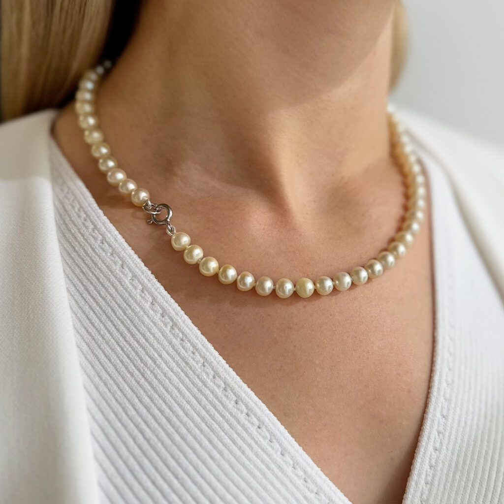 Perlenkette mit ca. 7–7,5mm unregelmäßigen Süßwasserperlen und schlichtem 925-Silber-Springring, 48cm lang, von einer elegant gekleideten jungen Frau getragen und in stilvoller Nahaufnahme präsentiert.