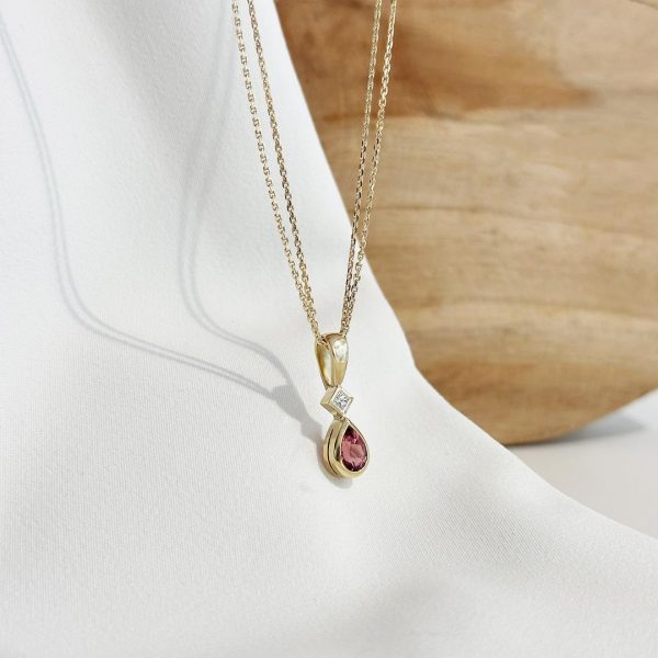Handgefertigter Goldanhänger mit Diamant und Turmalin, an filigraner Karree-Kette – Frontansicht vor eleganter Holzwand.