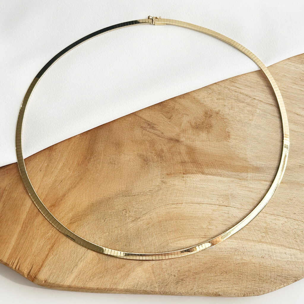 Halsreifen aus Gold liegt auf Holz und weißem Tuch