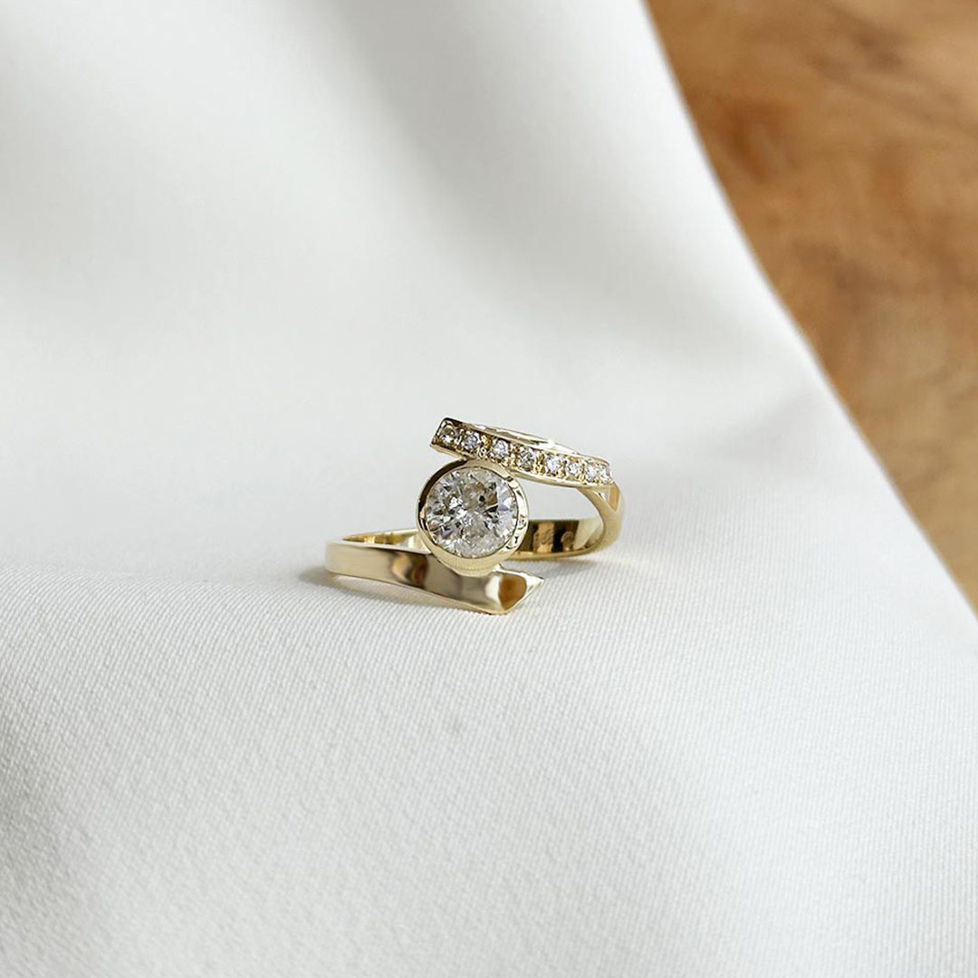 Schmuckanfertigung Ring mit geschwungener Ringschiene und Brillanten aus 585 Gelbgold fotografiert auf elegantem Stoff.