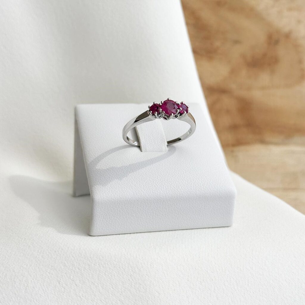 Ring aus 585er Weißgold mit drei roten Rubinen, seitlich auf Ringaufsteller fotografiert, Fokus auf die gestufte Rubin-Anordnung, die elegante Fassung und die zeitlose Linienführung