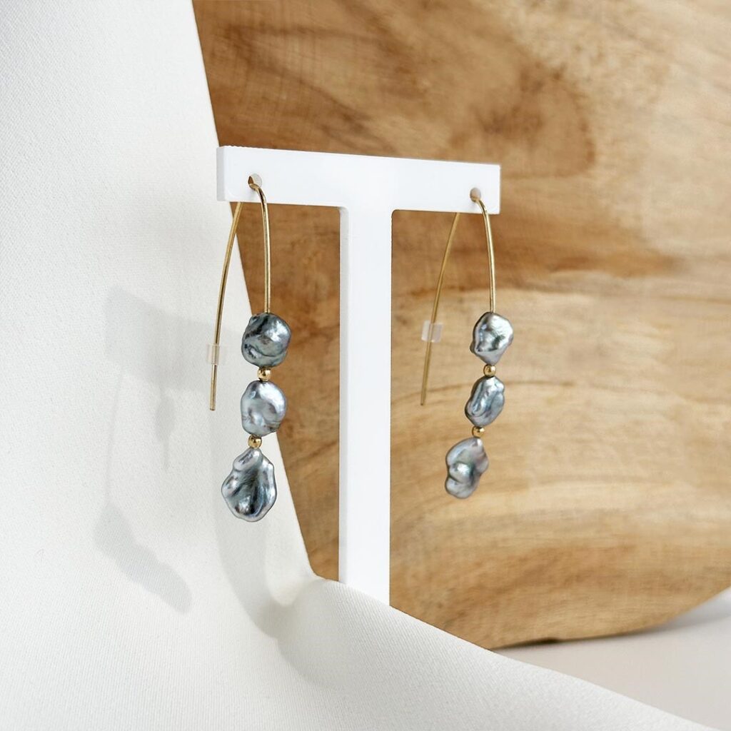 Elegante Ohrhaken aus 585er Gelbgold mit jeweils drei grau schimmernden Tahiti-Keshi-Perlen in leicht unregelmäßiger Form. Zwischen den Perlen sitzen kleine Goldkügelchen, die dezente Akzente setzen. Seitliche Nahaufnahme mit Fokus auf der natürlichen Struktur der Keshi-Perlen und der feinen Verarbeitung der Golddetails.