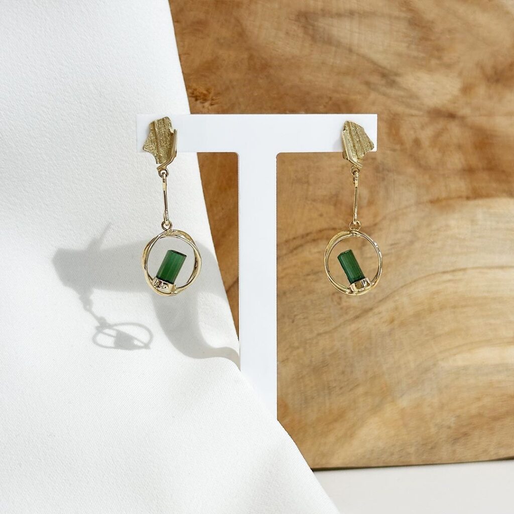 Handgefertigte Turmalin-Kristall-Ohrringe aus 585 Gelbgold vor Holzwand präsentiert.