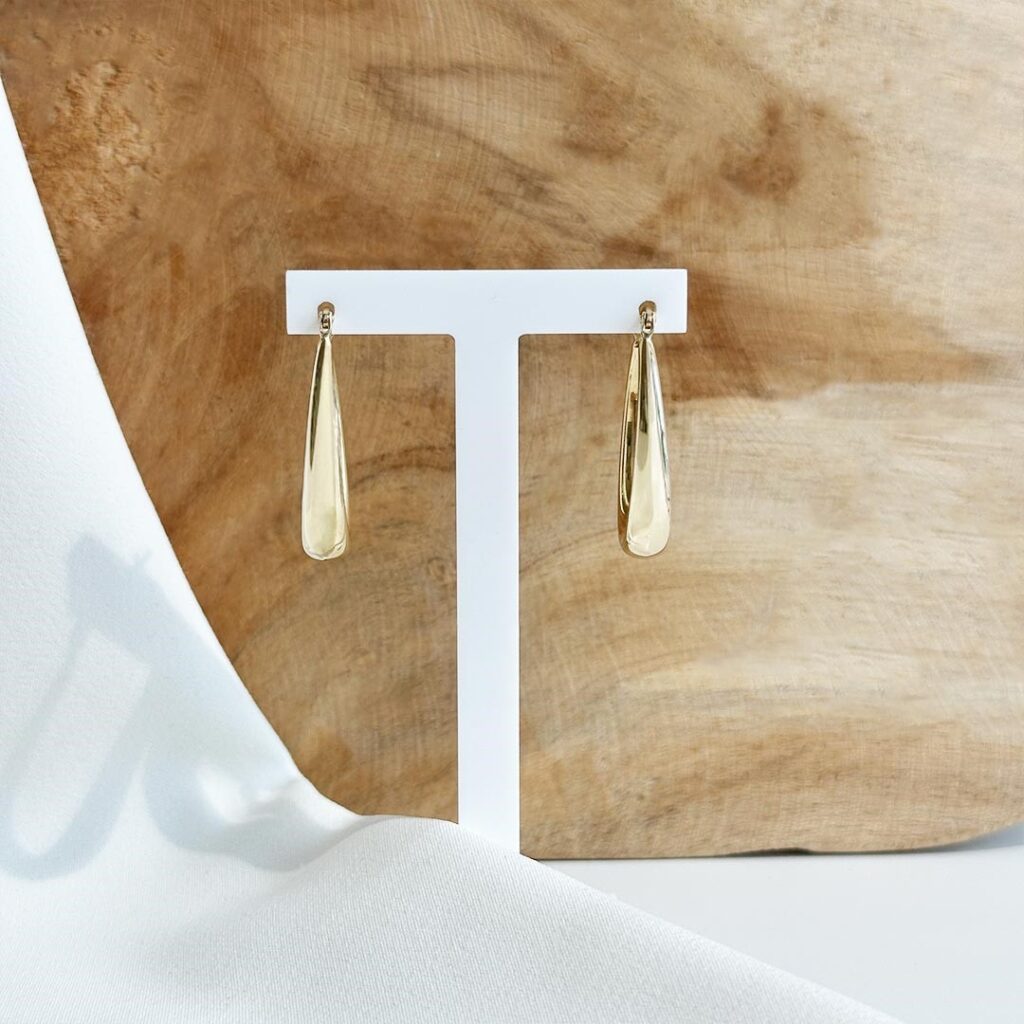 Oval geformte Creolen aus 585 Gelbgold in frontaler Ansicht, mit sanft nach unten hin breiter werdendem Design, vor einer Hozlwand von vorne präsentiert.