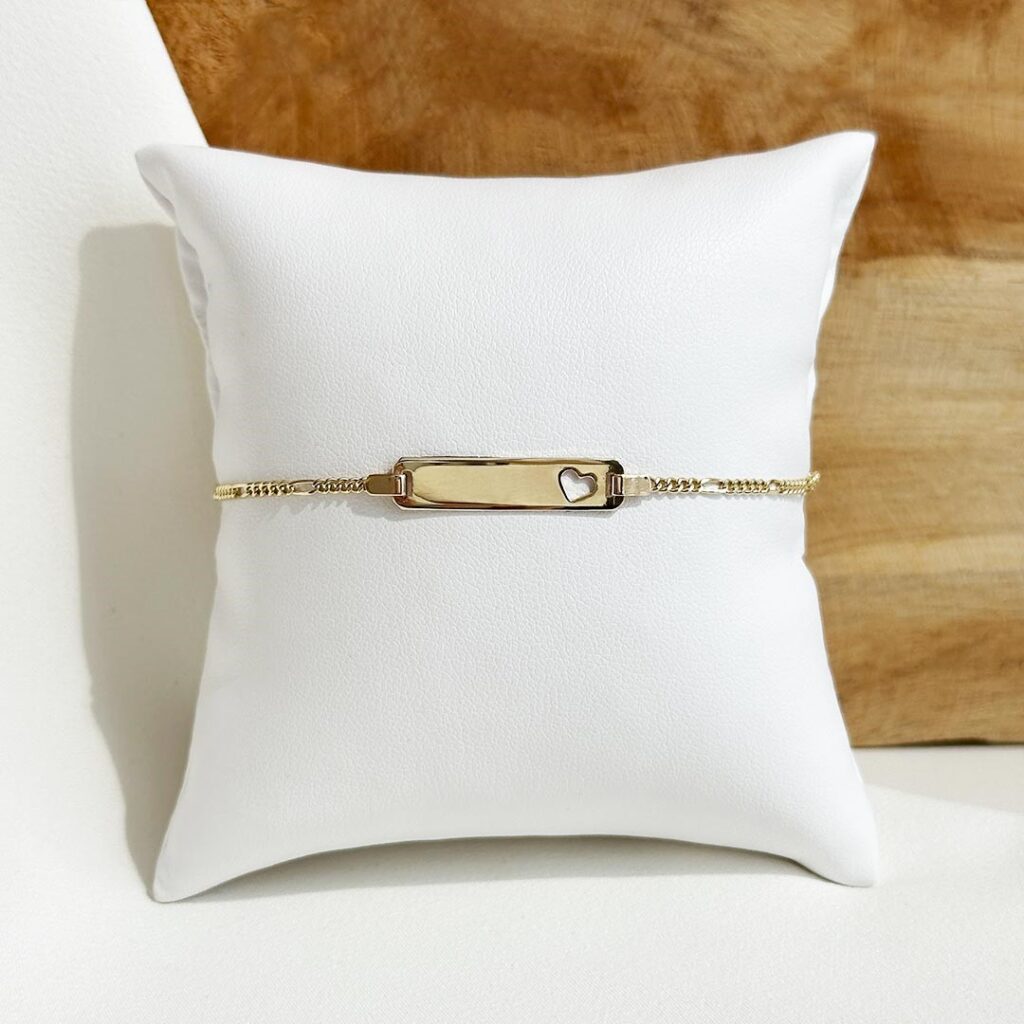 Zartes Schildarmband aus 585er Gelbgold mit feiner Figaro-Kette, 14cm lang mit Zwischenöse bei 12cm. Das längliche Schild (ca. 25x5mm) zeigt ein ausgestanztes Herz und bietet Platz für eine Gravur. Elegante, klare Nahaufnahme mit Fokus auf das Herzdetail.