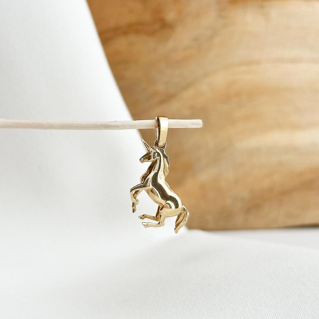 Einhorn-Anhänger aus 585 Gelbgold mit feinen Details und 20mm Größe, in eleganter Nahaufnahme vor einer Holzwand fotografiert.