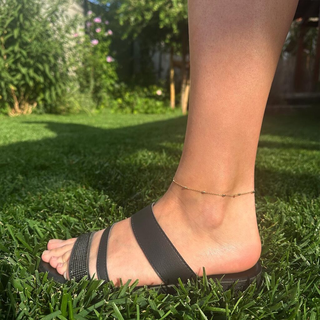 Zartes Fußkettchen aus 585er Gelbgold mit feiner Gliederkette, 26cm lang mit 3cm Verlängerung, filigran und sommerlich in Nahaufnahme in der Wiese fotografiert.