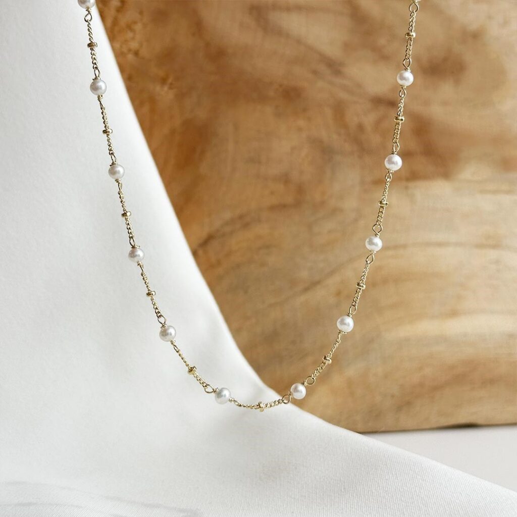 Zarte 585 Gelbgoldkette mit kleinen Süßwasserkulturperlen und polierten Goldkugeln, 40cm Länge plus 5cm Verlängerung, filigran und jugendlich in Nahaufnahme vor einer Holzwand gezeigt.