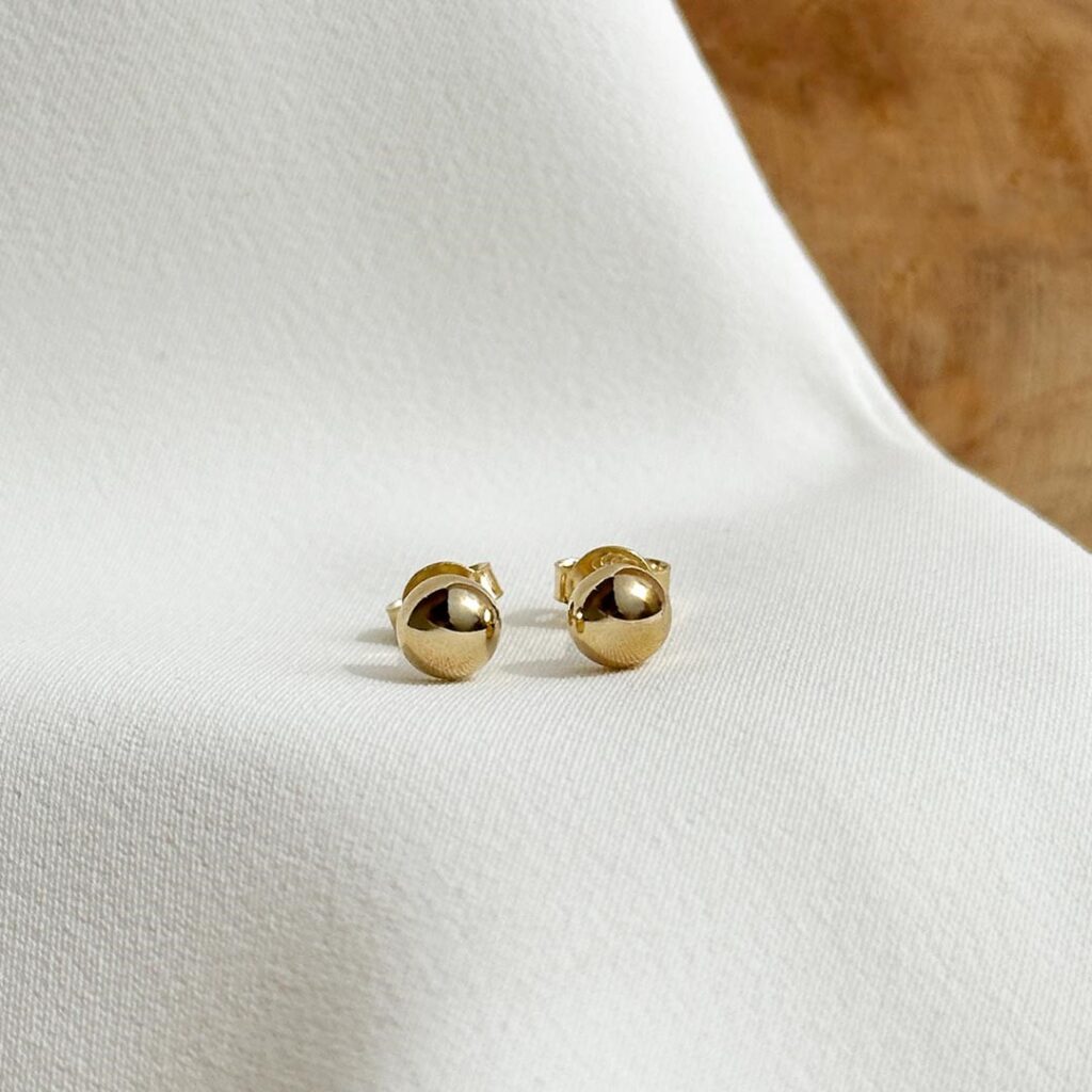 Halbkugel-Ohrstecker aus 585 Gelbgold mit 6mm Durchmesser, sanft gewölbter Oberfläche und warmem Glanz, in eleganter Nahaufnahme vor einer Holzwand fotografiert.