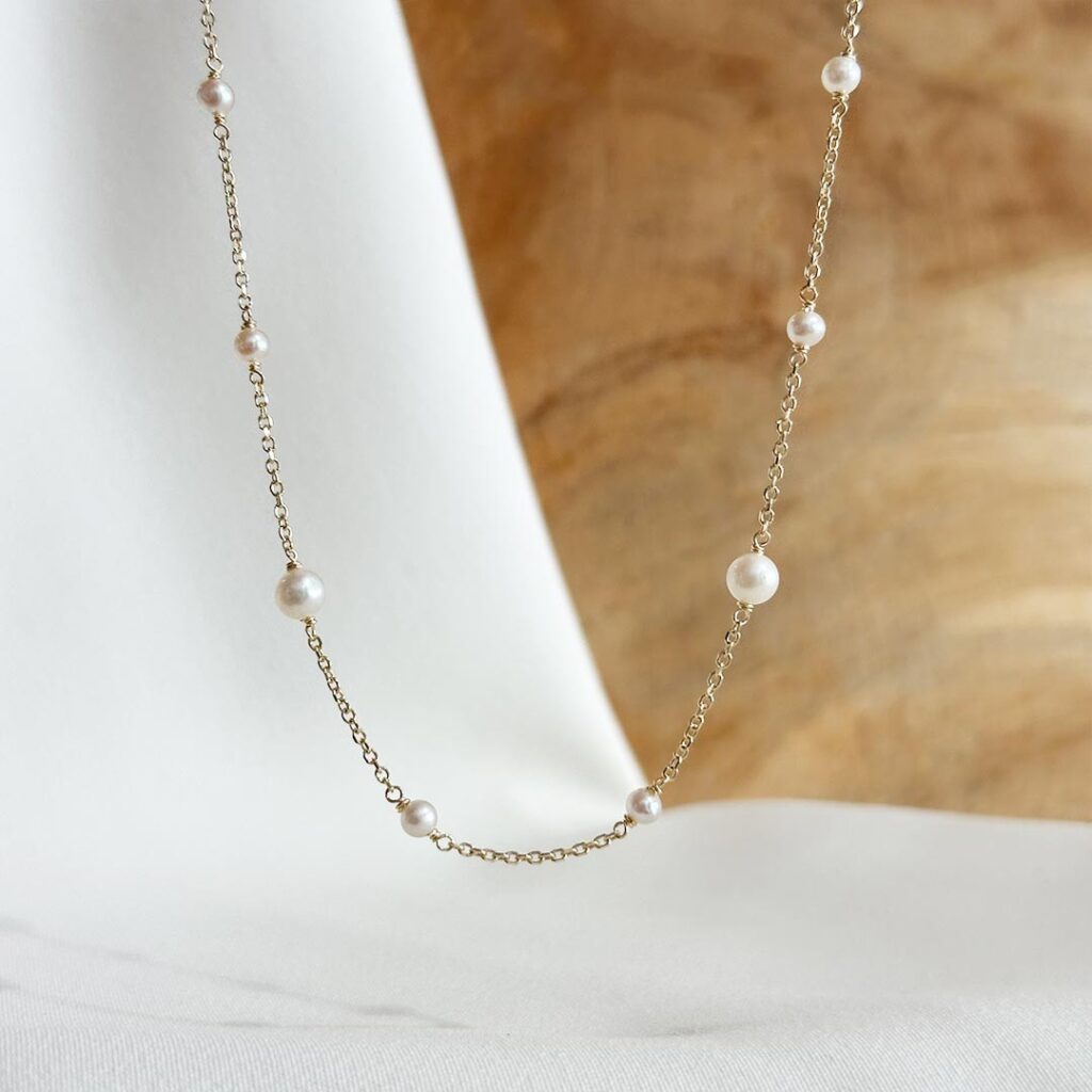 Zarte Goldkette aus 585er Gelbgold mit kleinen und größeren weißen Süßwasserperlen in regelmäßigen Abständen, 45cm Länge mit Zwischenöse bei 42cm, in eleganter Nahaufnahme präsentiert.