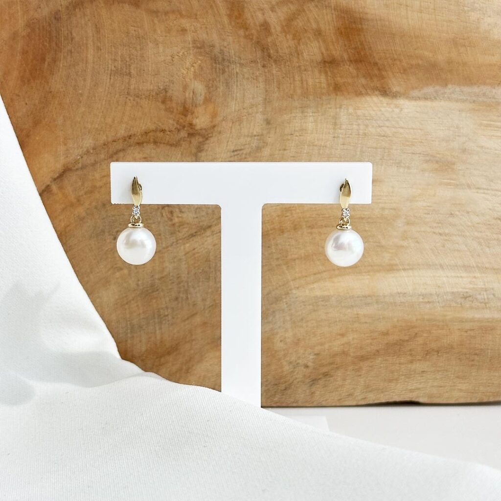 Ohrstecker aus 585er Gelbgold mit zart schimmernder Süßwasserperle und kleinem funkelnden Diamanten darüber, in eleganter Nahaufnahme präsentiert.