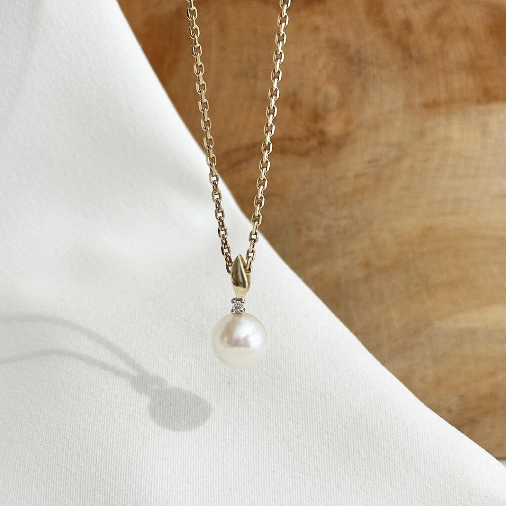 Anhänger aus 585 Gelbgold mit zart schimmernder Süßwasserperle und kleinem funkelnden Diamanten darüber, in eleganter Nahaufnahme präsentiert.