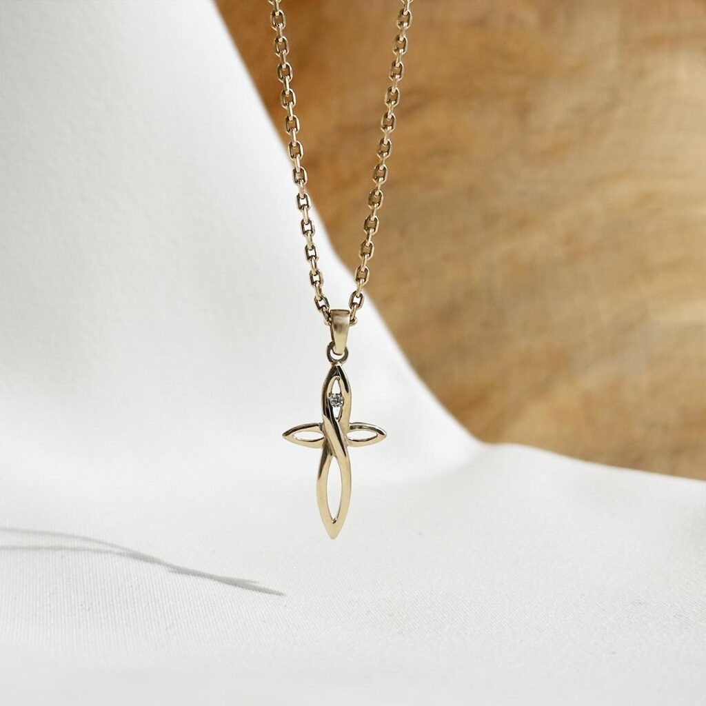 Modern gestalteter Kreuzanhänger aus 585er Gelbgold mit geschwungenen Linien, durchbrochener Mitte und mittig gefasstem farblosem Zirkonia auf einer Goldkette, in eleganter Nahaufnahme präsentiert.