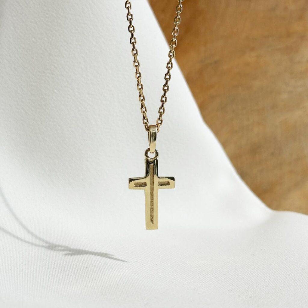 Modernes Kreuz aus 585er Gelbgold, 20mm lang, mit feiner vertiefter Linienstruktur über beide Balken, an einer Goldkette in eleganter Nahaufnahme präsentiert.