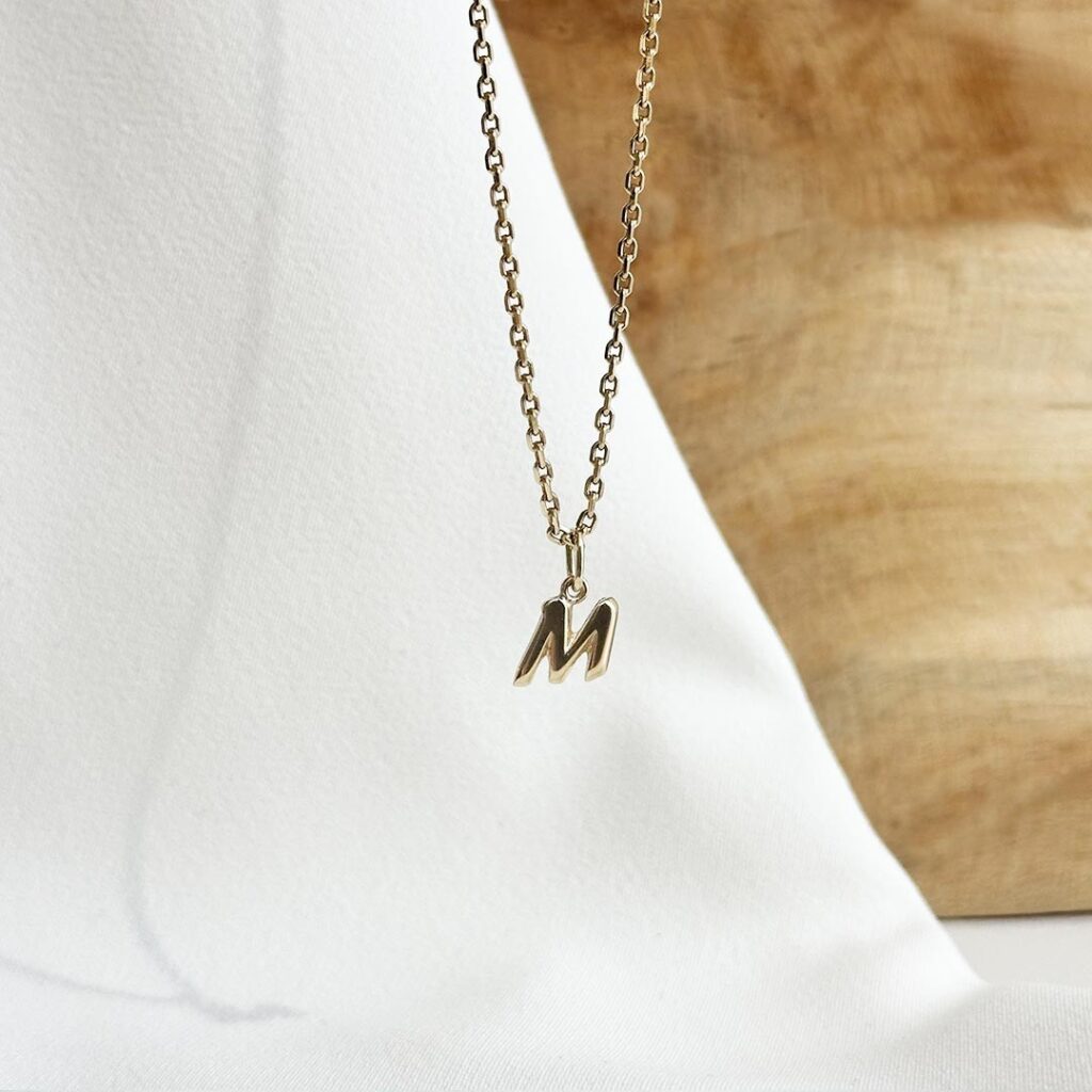 Buchstabe-M-Anhänger aus 585 Gelbgold, 10mm groß, mit polierter Oberfläche, an einer zarten Goldkette in eleganter Nahaufnahme präsentiert.