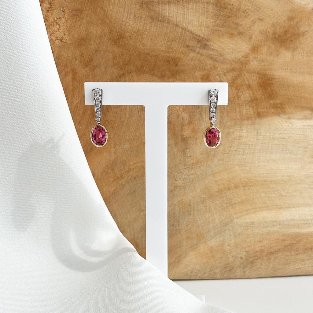 Handgefertigte Ohrgehänge aus 585 Gelbgold und Weißgold, 20mm lang, mit abgestuft gefassten Brillanten am Stecker und ovalem rosa-rot schimmerndem Turmalin in glatter Gelbgoldfassung, in eleganter Nahaufnahme präsentiert.