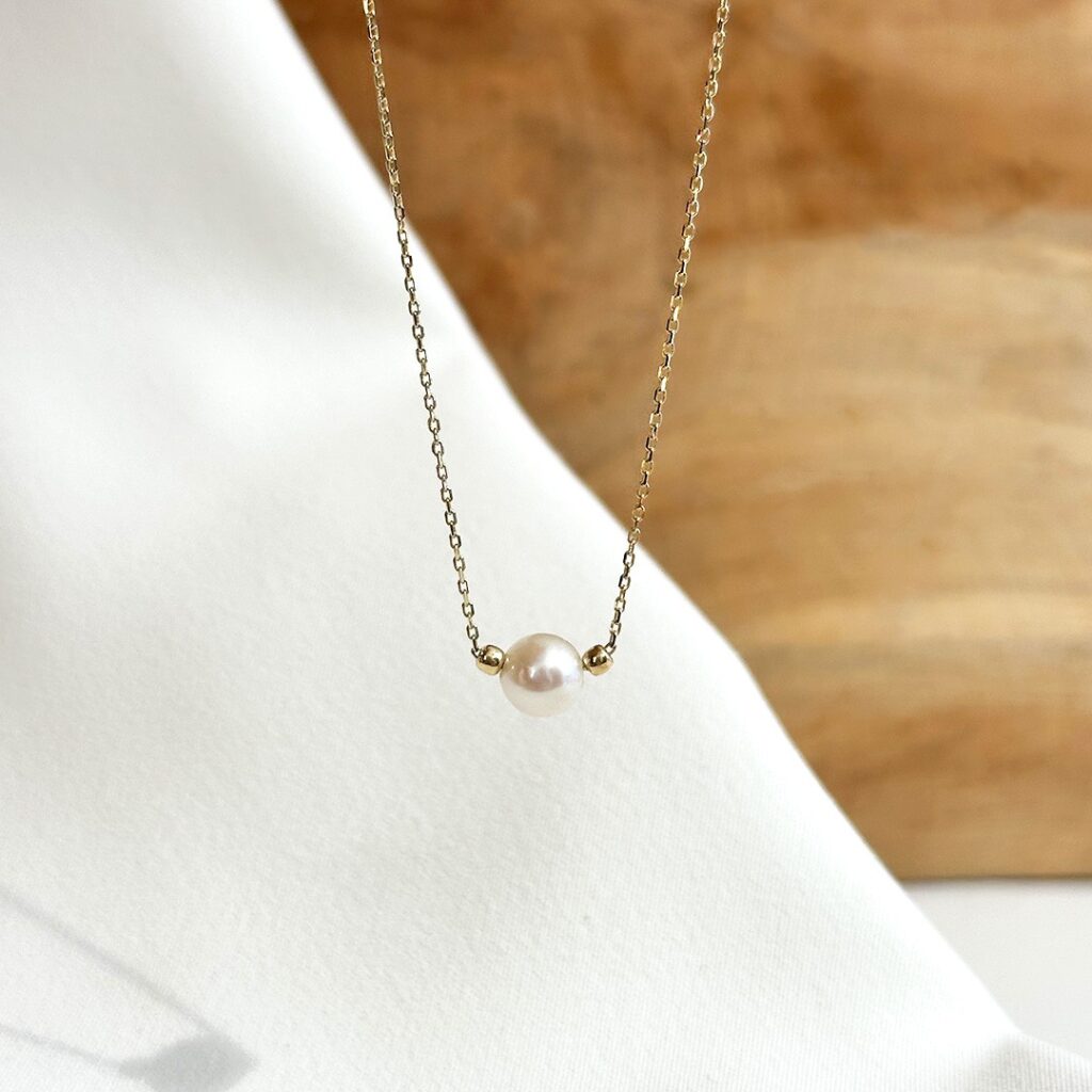 Feines Collier aus 585er Gelbgold mit 6mm Süßwasserperle und kleinen Goldkügelchen, an einer 45cm Kette mit Zwischenöse bei 42cm elegant in Nahaufnahme präsentiert.