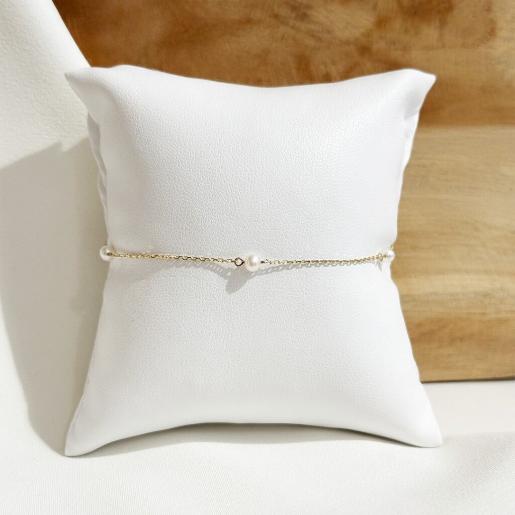 Armband aus 585er Gelbgold mit feiner Gliederkette und zarten, regelmäßig eingearbeiteten Süßwasserperlen, 19cm lang, in eleganter Nahaufnahme vor einer Holzwand präsentiert.