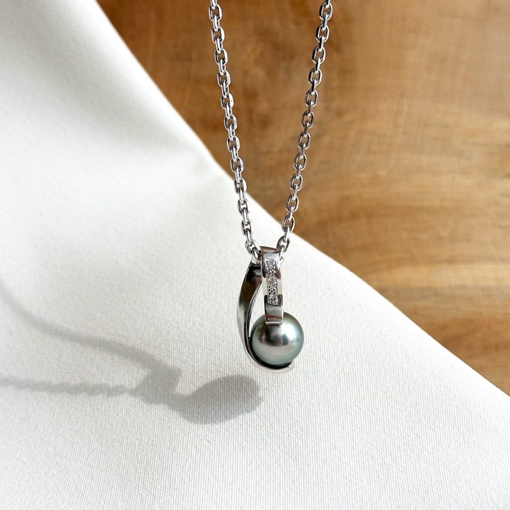 Anhänger aus 585er Weißgold mit schimmernder Tahitiperle und drei kleinen Brillanten in der geschwungenen Schlaufe, in eleganter Frontansicht präsentiert.