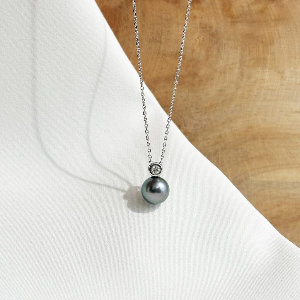 Anhänger aus 585 Weißgold mit dunkler Tahiti-Perle und rund gefasstem 0,05ct. Brillanten, in Nahaufnahme an einer feinen Kette präsentiert.