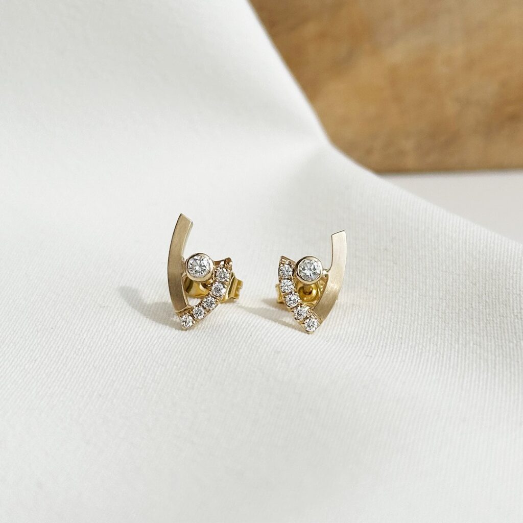 Handgefertigte Ohrstecker in V-Form aus Gold mit mattierten und polierten Flächen, Brillanten und rund gefasstem Mittelstein.