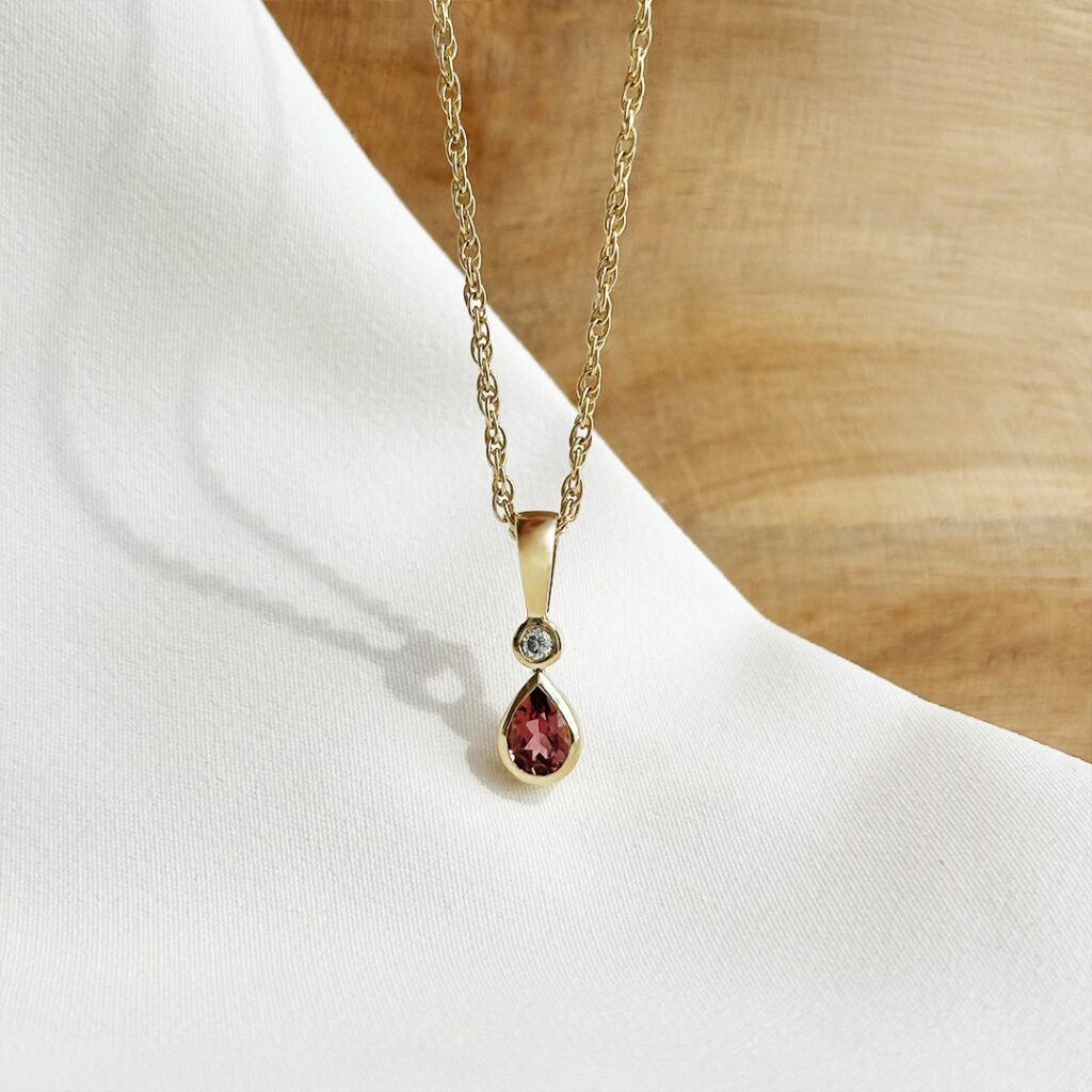 Anhänger aus 585er Gelbgold mit rund gefasstem Brillanten und rosafarbenem Turmalin im Tropfenschliff, fotografiert an einer feinen Goldkette.