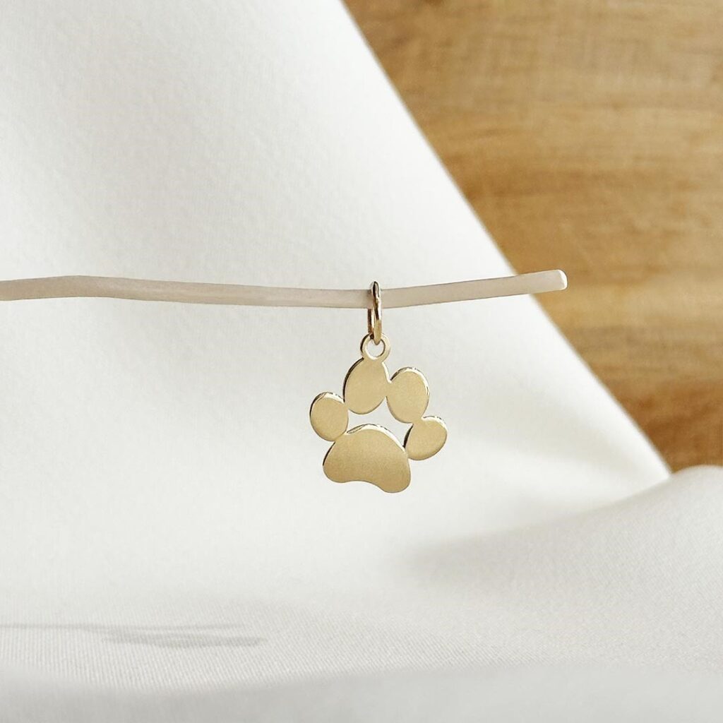 Anhänger in Form einer Hundepfote aus 585er Gelbgold, ca. 15mm groß, für eine Halskette oder ein Bettelarmband und in eleganter Nahaufnahme gezeigt.