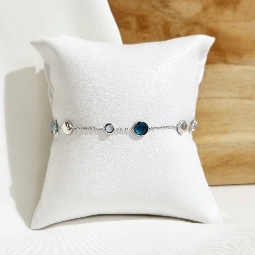 Armband aus 585er Weißgold mit abwechselnd hellen und dunklen Blautopasen, elegant auf einem Schmuckpolster präsentiert.