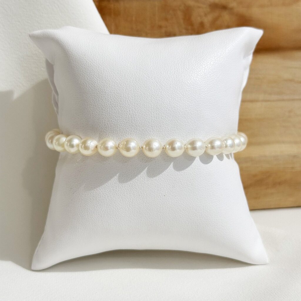 Klassisches Perlenarmband aus gleichmäßig runden Akoyaperlen, elegant auf Schmuckpolster präsentiert, Fokus auf den sanften Lüster der Perlen und die harmonische Reihung
