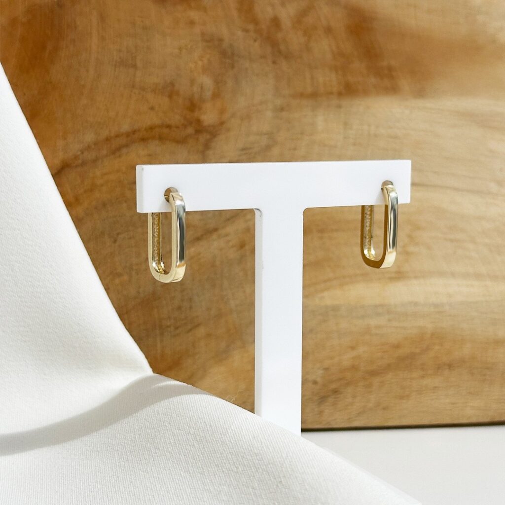 Ovale Creolen aus 585er Gelbgold, ca.14mm groß, leicht seitlich auf Schmuckaufsteller fotografiert, Fokus auf die kantige Linienführung und die moderne, reduzierte Form