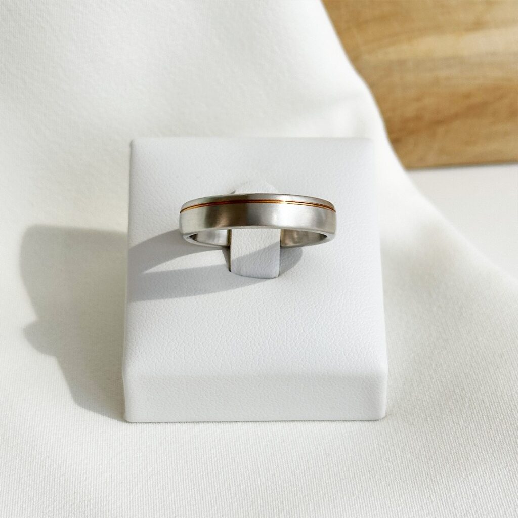 Ring aus 950er Platin mit feiner Rille aus 750er Gelbgold, frontal fotografiert, Fokus auf die matte Platinoberfläche, den warmen Goldakzent und die klare Linienführung