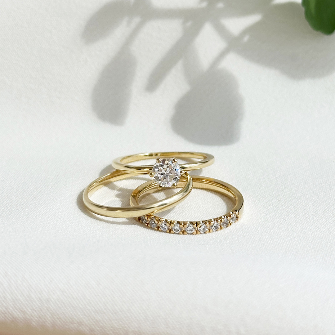 Eheringe aus Gelbogld: Ringkombination aus Verlobungsring, Memoire-Ring und Ehering aus Gelbgold, elegant auf Stoff liegend fotografiert,