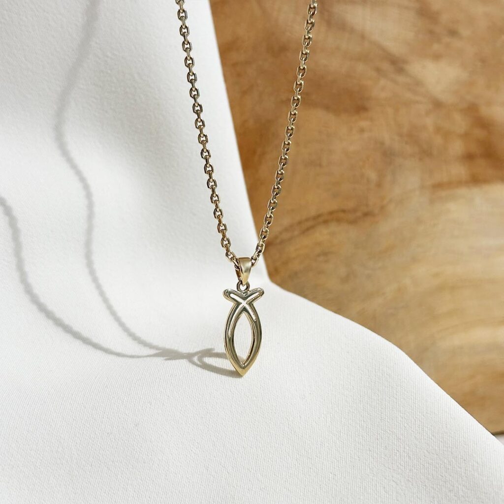 Ichthys-Fisch Anhänger aus 585er Gelbgold, ca.18mm groß, hängend an einer feinen Goldkette vor einer eleganten Holzwand fotografiert, Fokus auf die klassische Fischform und die symbolische Bedeutung des christlichen Glaubens, beliebtes Geschenk zur Taufe oder Erstkommunion.