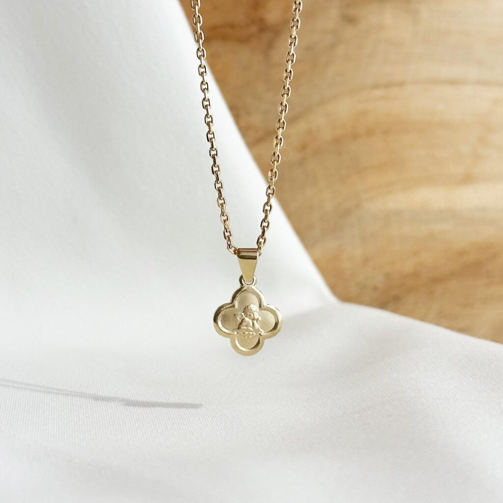 Schutzengel Anhänger aus 585er Gelbgold in Kreuzform, 10mm groß, hängend an einer feinen Goldkette vor einer eleganten Holzwand fotografiert, Fokus auf den kleinen Engel, den polierten Rand und die matte Oberfläche, beliebtes Geschenk zur Taufe oder Geburt